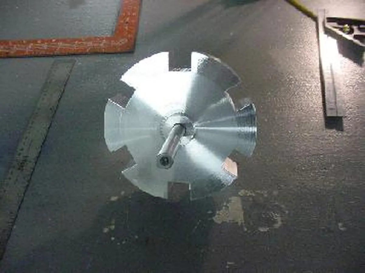 A top view of a metallic custom part with a gear-like design, showcasing its polished surface and central shaft